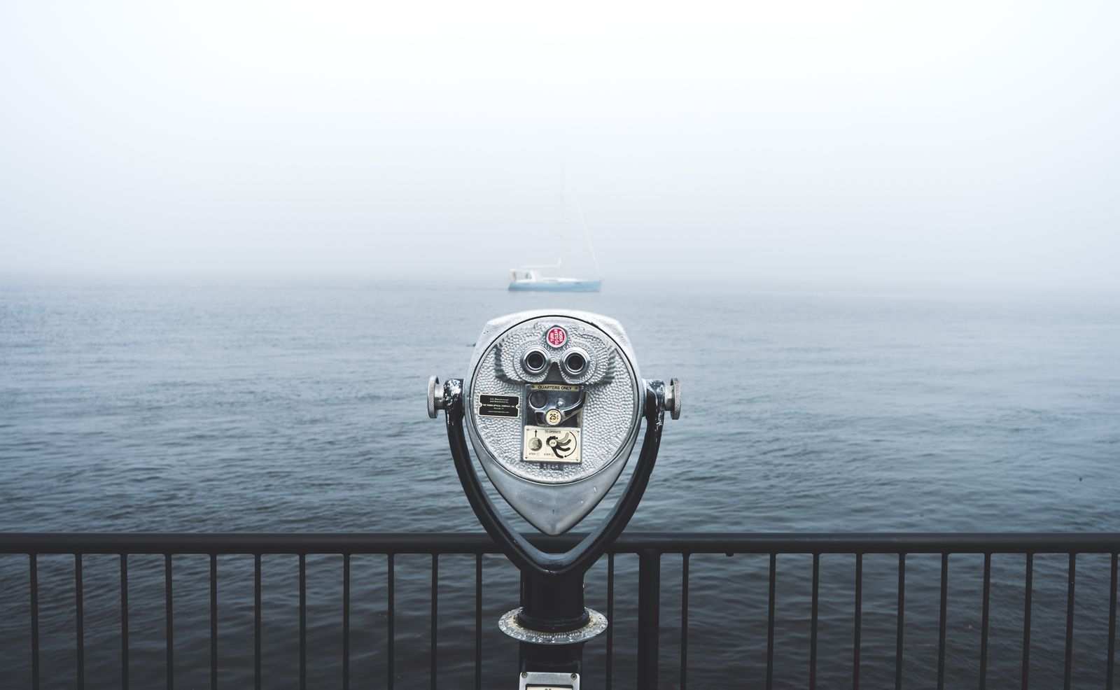 schip-niet-zichtbaar-pexels-1136815 Verrekijker op een kade met zicht op zee in de mist, met in de verte een zeilboot